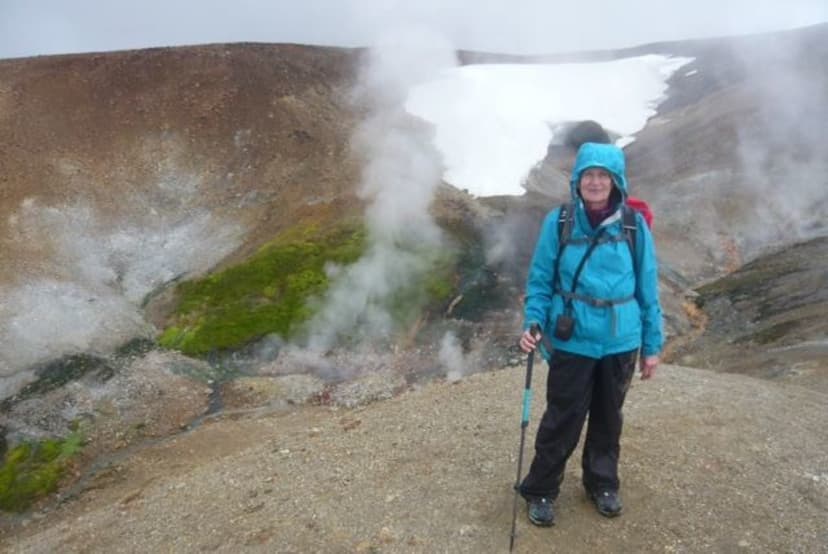 A hiker in a blue jacket standing on a ridge beside a steaming geothermal area in the Icelandic highlands