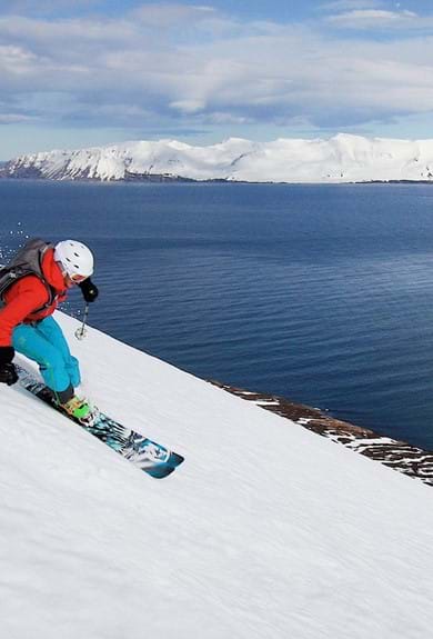 A person skiing down a mountain in Iceland with the ocean next to it