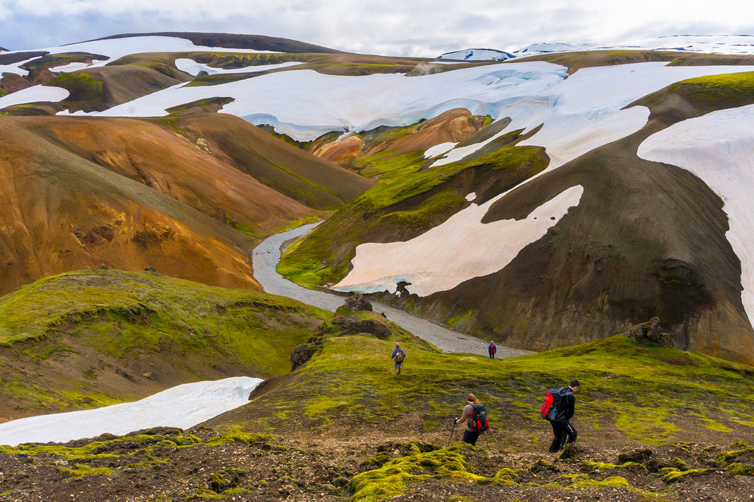 Hikers walking in colorful landscapes, surrounded by hills colored green, yellow, brown, and white