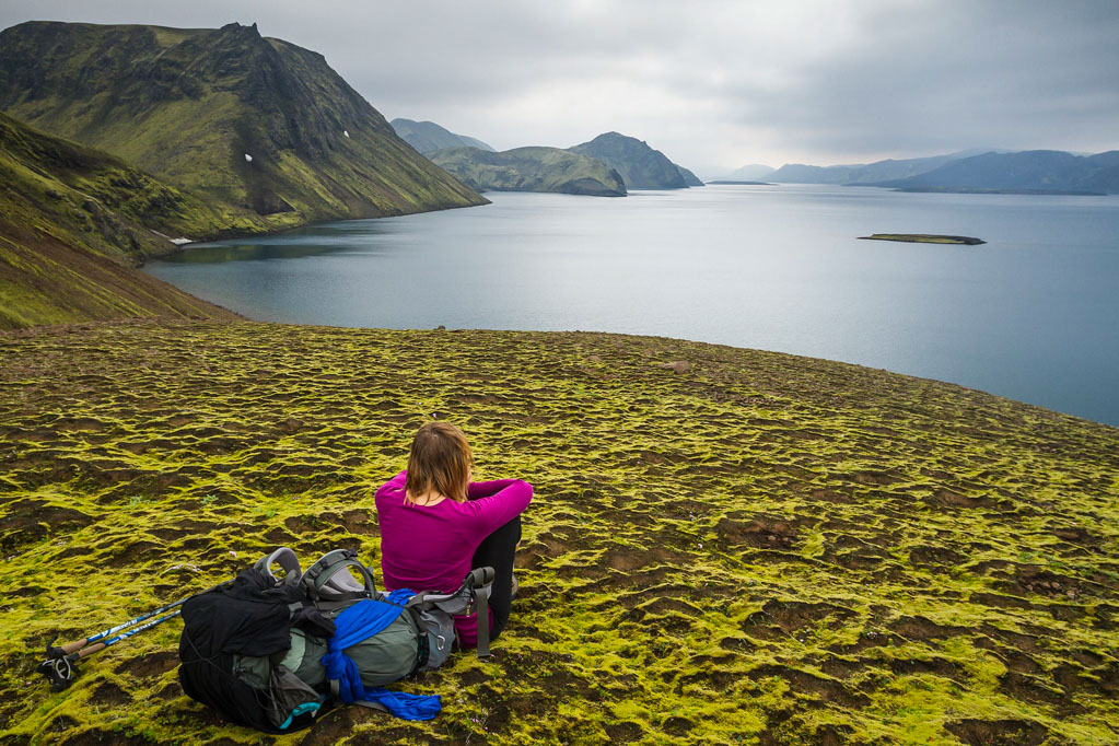 A solo female hiker sitting on the green moss, admiring the view from a viewpoint