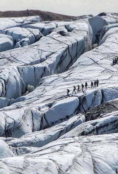 An aerial shot of a Falljokull in Iceland where a group on a glacier hike is finding its way through the cracked white surface in the distance